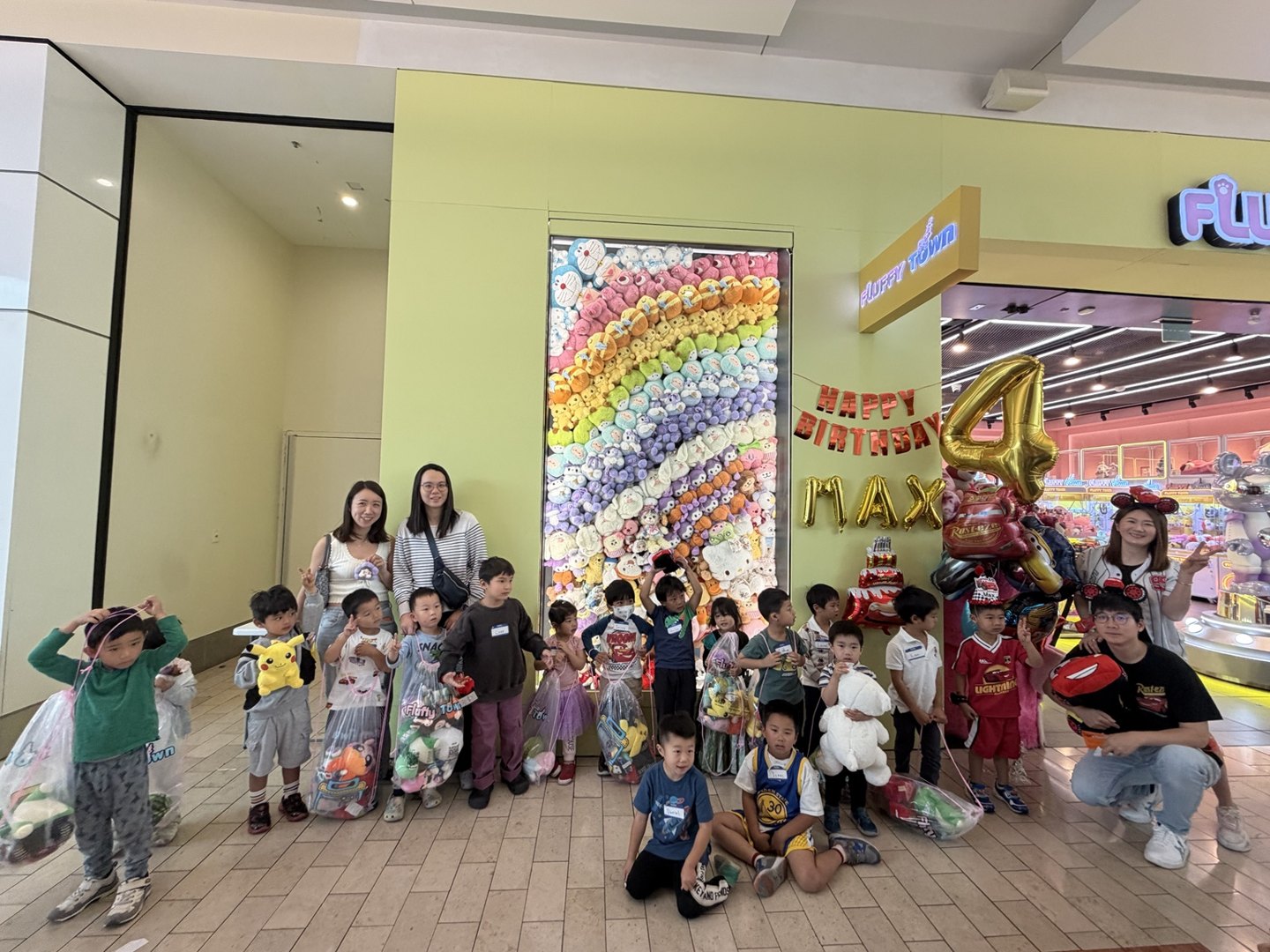 Children and families posing together beside a decorated birthday table and colorful plush wall