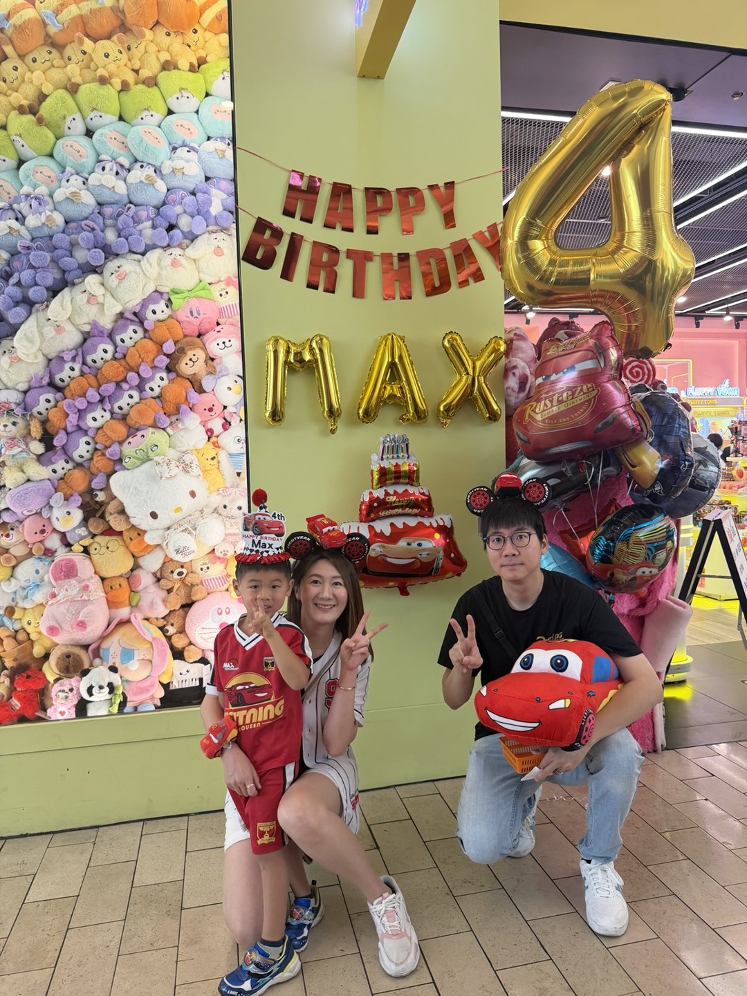 A decorated birthday table with a cake, birthday banner and gold number balloon beside the Rainbow Plush Wall
